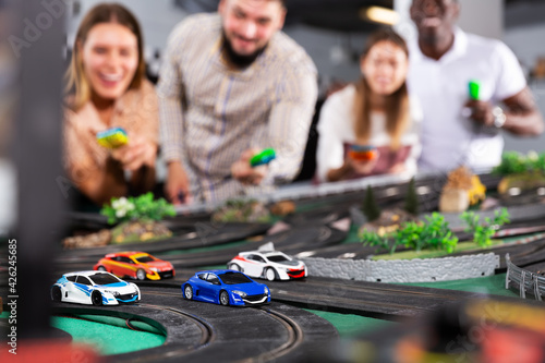 Models of race cars on the track in playroom, team of emotional players on background