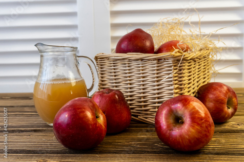 Red apples in a basket and apple juice in a jug on a wooden table