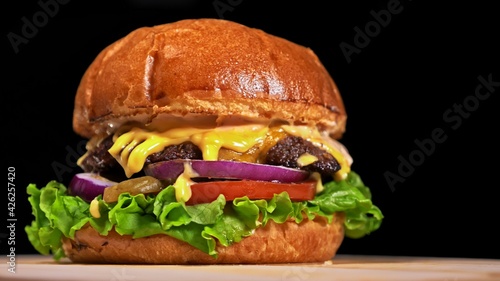 Craft burger is cooking on black background. Consist: sauce, lettuce, tomato, red onion, pickle, cheese, bacon, air bun and marbled meat beef.