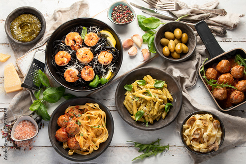Assortment of Italian pasta with traditional snacks and sauces for dinner on white wooden background.
