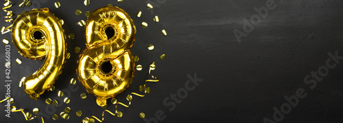 golden foil balloon number ninety eight. Birthday or anniversary card with the inscription 98. Black concrete background. Anniversary celebration. Banner. © mtrlin