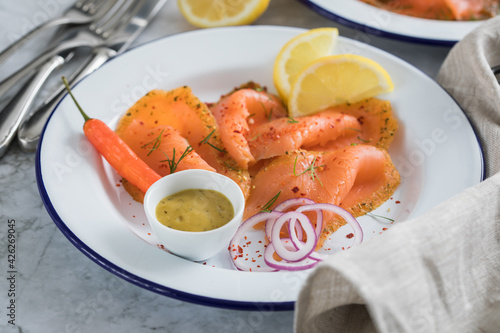 Asia Art Gravlax Graved Lachs, ein roh gebeizter Fisch mit Zitronengras und Chili auf Emaille Teller mit Hovmästarsås Senf Soße, Toast, Zwiebel Ringe, Dill, Zitrone und Leinen Tuch auf hell Marmor 