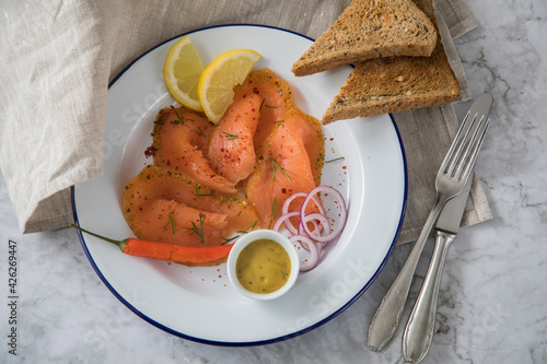 Asia Art Gravlax Graved Lachs, ein roh gebeizter Fisch mit Zitronengras und Chili auf Emaille Teller mit Hovmästarsås Senf Soße, Toast, Zwiebel Ringe, Dill, Zitrone und Leinen Tuch auf hell Marmor Hin