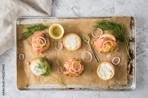 Gravlax Graved Lachs, ein roh gebeizter Fisch mit Dill auf Brötchen mit Frischkäse, Hovmästarsås Senf Soße, Zwiebelringe, auf Backblech mit Backpapier und hell Marmor Hintergrund photo