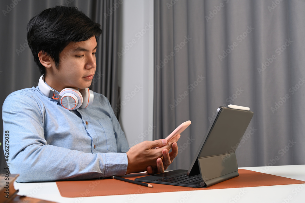 Casual asian man with headphone sitting in front of his computer tablet and using smart phone. Casual asian man with headphone sitting in front of his computer tablet and using smart phone.
