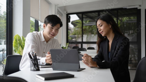 Two happy businesswoman using computer tablet and discussing business idea in modern office.