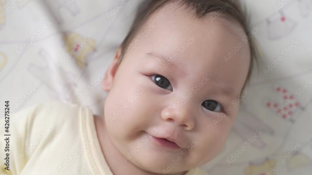 asian baby infant laying down on white soft bed happy and smile. 3 months old baby facial laughing expression. asian baby infant laying down on white soft bed happy and smile. 3 months old baby facial laughing expression.