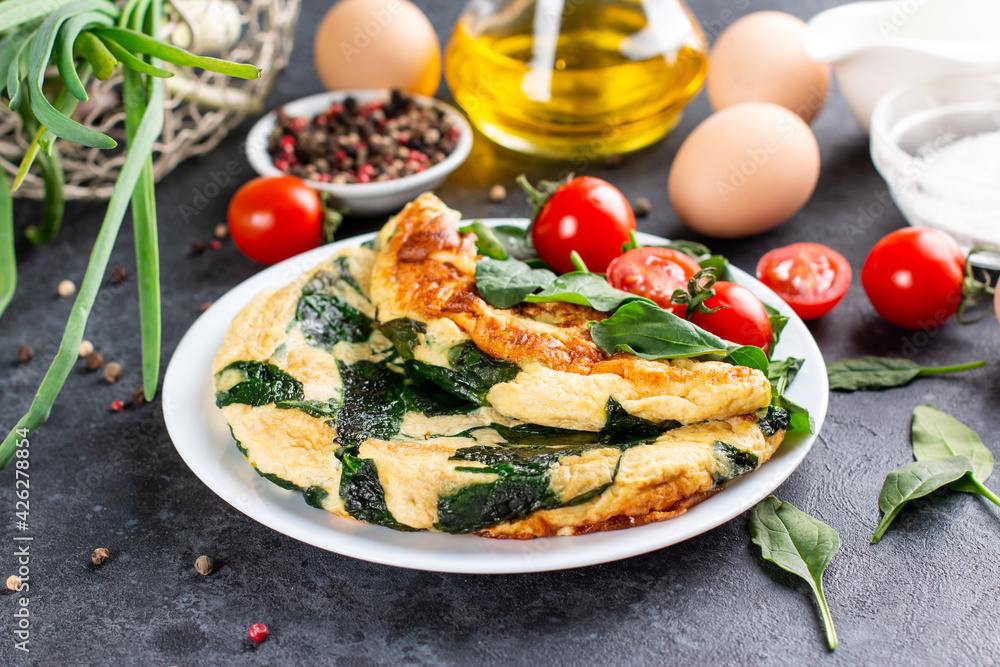 Omelet with spinach leaves. Omelette on plate, scrambled eggs on a dark slate or concrete background.