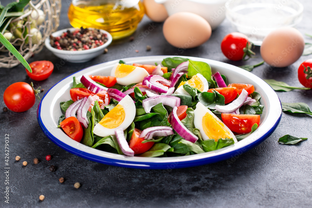 Delicious salad of spinach, boiled egg, tomatoes, nuts and spices on a dark slate, stone or concrete background.