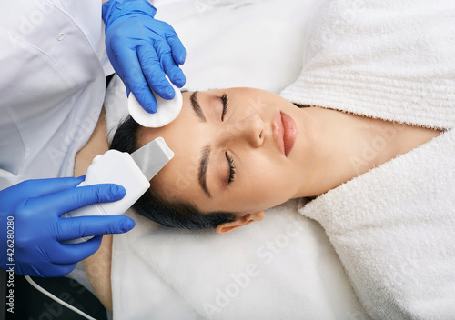 Ultrasound facial peeling. Brunette woman getting ultrasonic peel skin with skin scrubber at cosmetology clinic photo