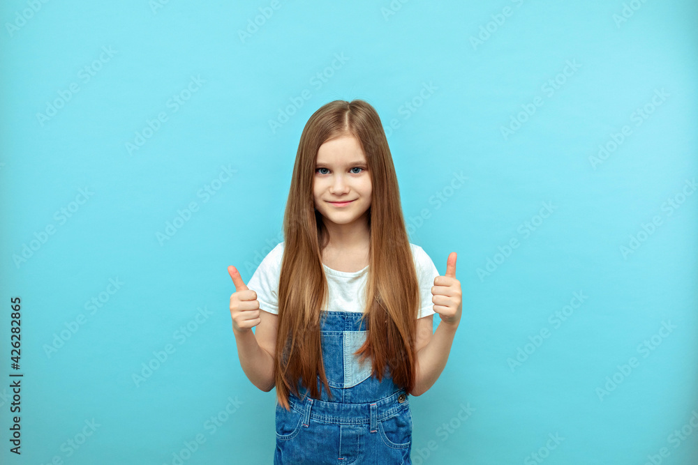 Fototapeta premium Beautiful little girl holds her fingers in the top. Expressive facial expressions are the emotions of a satisfied child.