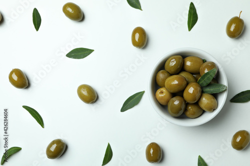 Bowl of green olives and leaves on white background, top view