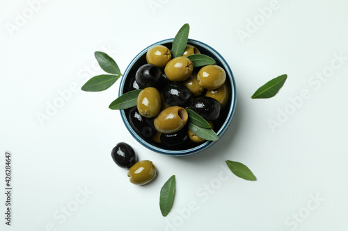 Bowl of olives and leaves on white background, top view