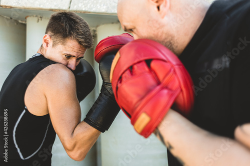 Two men exercising and fighting in outside. Boxer in gloves is training with a coach © xartproduction