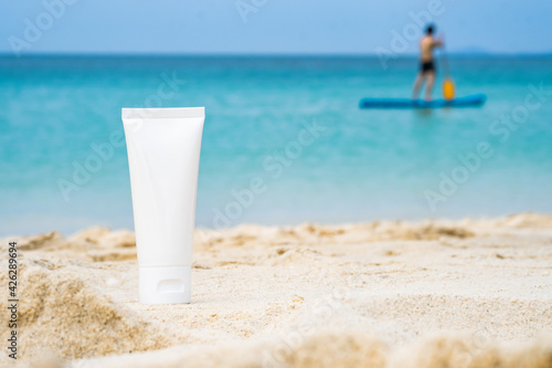 empty cosmetic skin care cream or sun block on sand beach with sea side and people relax on the beach background travel vacation accessory 