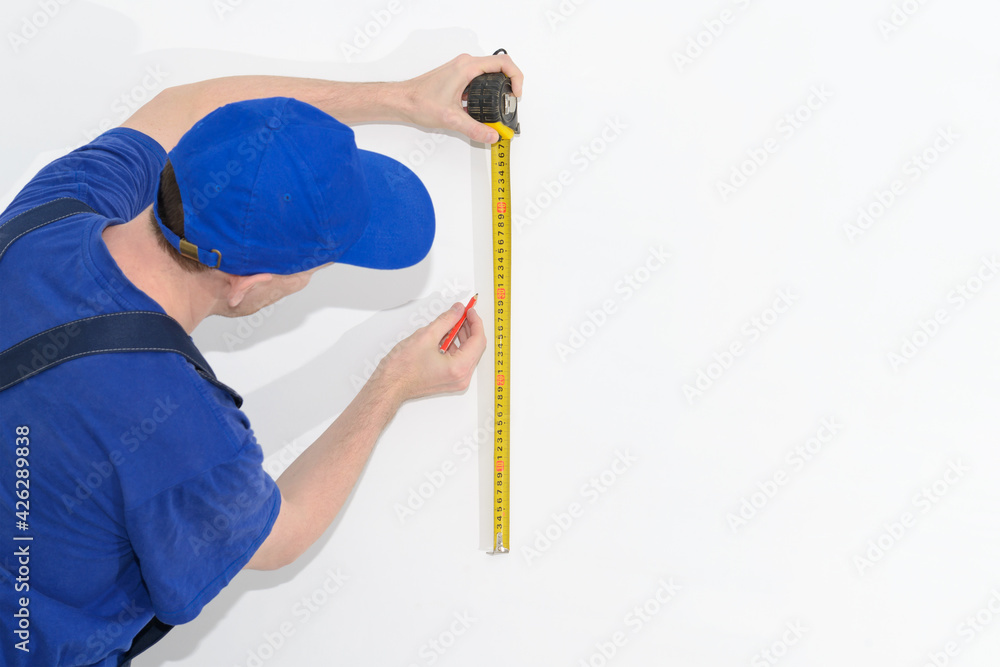 uniformed worker measures with a tape measure on a white wall uniformed worker measures with a tape measure on a white wall