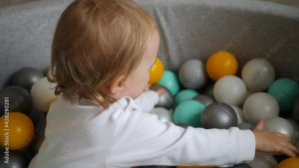 girl in a white bodysuit plays with colorful plastic balls in dry pool girl in a white bodysuit plays with colorful plastic balls in dry pool