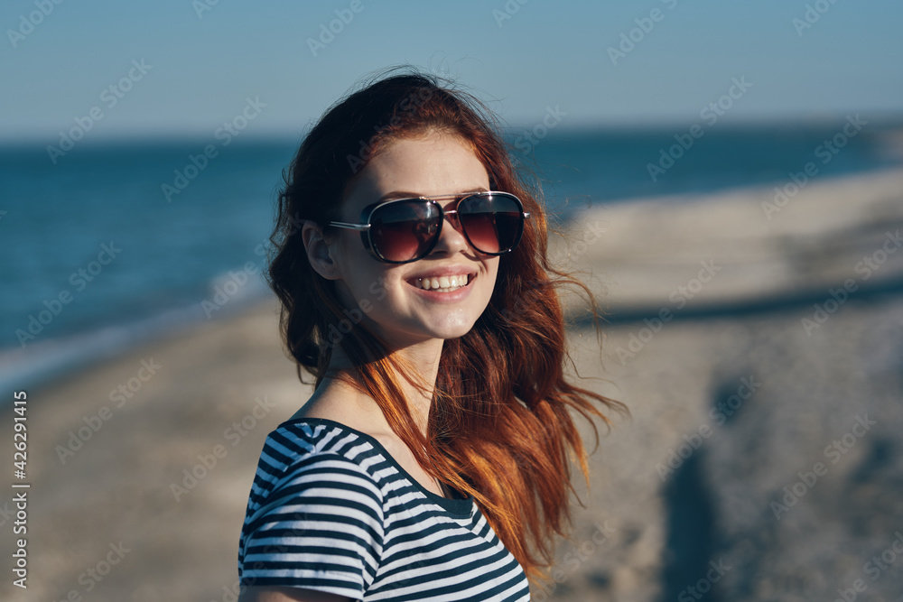 red-haired woman in the mountains in nature in glasses gestures with her hands on the beach near the sea red-haired woman in the mountains in nature in glasses gestures with her hands on the beach near the sea