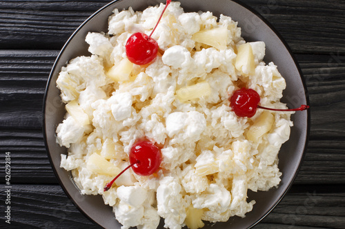 Foto American dessert salad consisting of rice, marshmallows and pineapple dressed with whipped cream close-up in a plate on the table