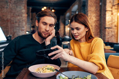 a woman in a sweater with a mobile phone and a guy with a beard are sitting in a restaurant