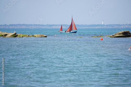 sailing boat on the sea with red sails on the island of Noimoutier, France by the lighthouse