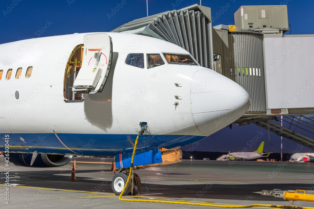 Passenger jet plane with open door stands at the air bridge connected to an external power supply on an airport night apron. Passenger jet plane with open door stands at the air bridge connected to an external power supply on an airport night apron.