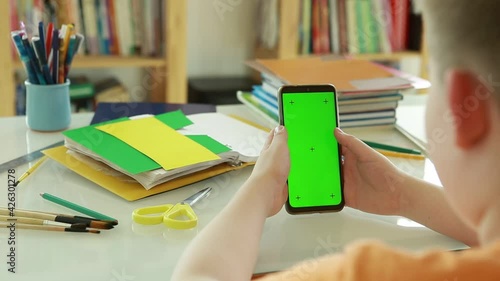 Phone with Green Screen and Chroma Key in the hands of a Primary school student.An elementary school student uses online videos to learn.   Schoolboy Scroll Up Cellphone by Finger.  
