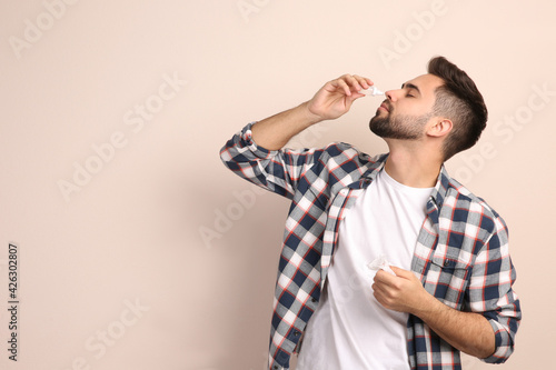 Man using nasal spray on beige background, space for text