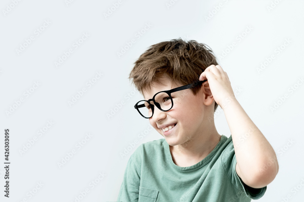 Surprised boy in a green T-shirt and glasses pensive scratches his head. Copy space.