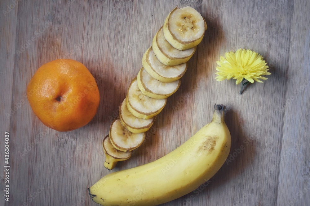 open and sliced banana and yellow flower, orange floating isolated on wooden board open and sliced banana and yellow flower, orange floating isolated on wooden board