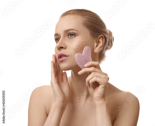 Beautiful young woman doing facial massage with gua sha tool on white background