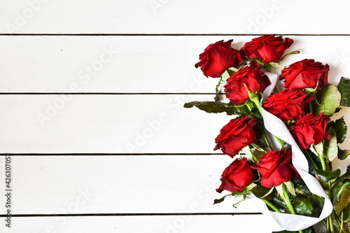 Red roses with white ribbon on a white wooden background. Greeting card. Copy space. Flat lay. Mothers day valentines day womans day concept.