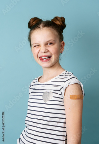 Portrait little girl with adhesive plaster on shoulder posing isolated. Covid-19 prevention
