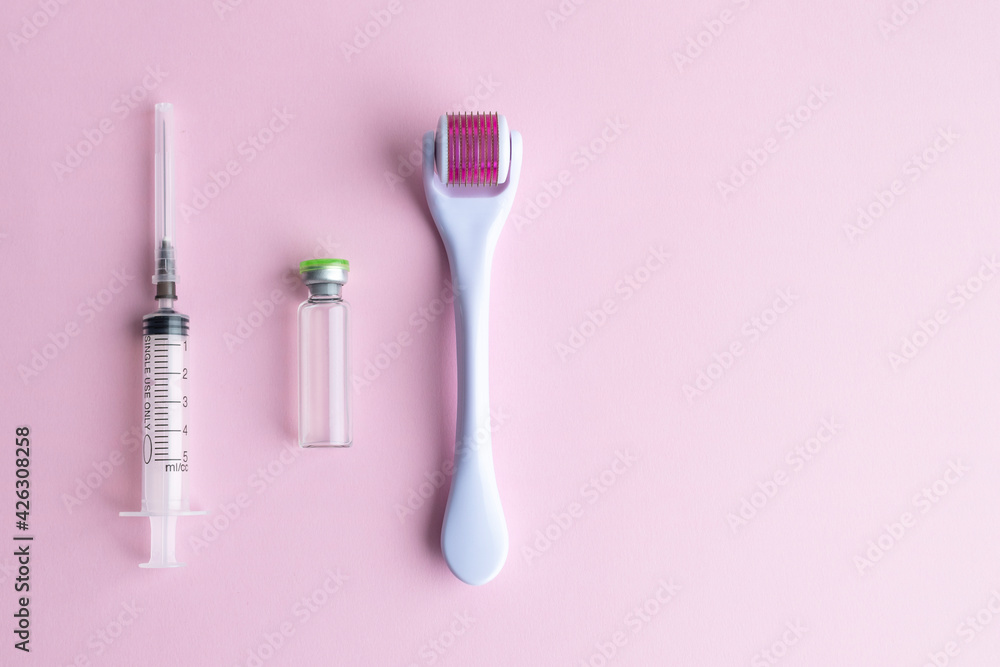 Dermaroller, mesoscooter, gold microneedles, hyaluronic acid ampoule and syringe on a pink background.Anti-aging skin care for the face, neck and décolleté area, anti-cellulite effect, hair strengthen Dermaroller, mesoscooter, gold microneedles, hyaluronic acid ampoule and syringe on a pink background.Anti-aging skin care for the face, neck and décolleté area, anti-cellulite effect, hair strengthen