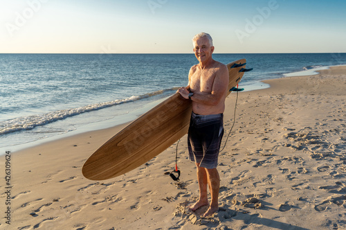 Photography Portrait of mature senior Surfer looking at the ocean with vintage surfboard on