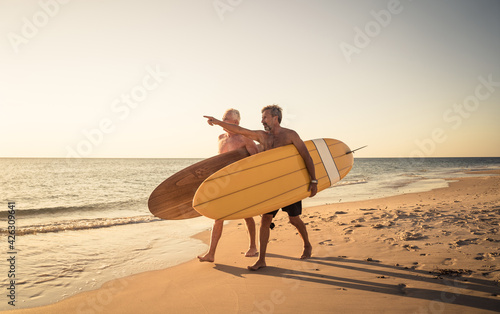 Photography Two senior surfers with surfboard having fun on empty remote beach enjoying reti
