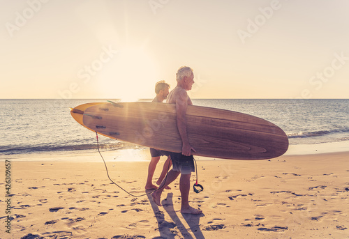 Photography Two senior surfers with surfboard having fun on empty remote beach enjoying reti