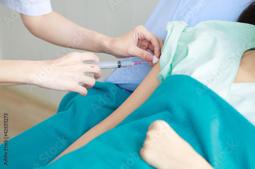 Asian young long hair female patient wears green hospital uniform covered by blanket lay down on blue pillow bed feel pain when doctor shot medicine injection by needle and syringe into right arm