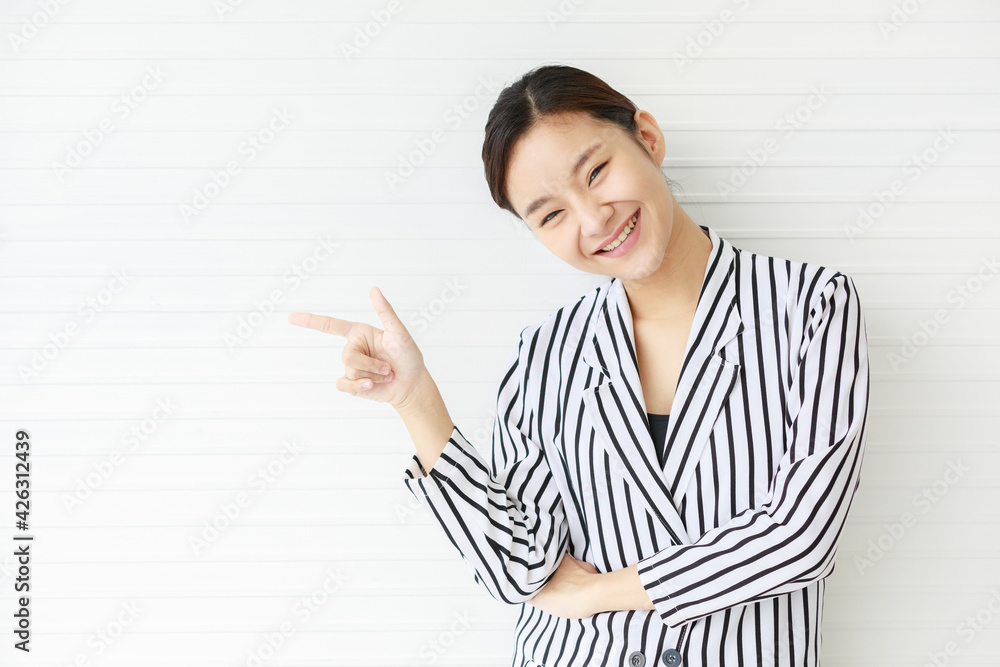 Portrait shot of Asian young confident happy female businesswoman wears black white stripe casual suit stand in front wall smiling hold hands point finger on empty copy space with cheerful face. Portrait shot of Asian young confident happy female businesswoman wears black white stripe casual suit stand in front wall smiling hold hands point finger on empty copy space with cheerful face.