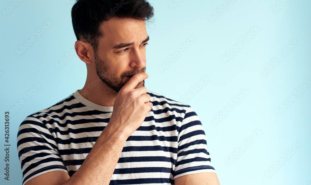Portrait of a worried young man looking at on side posing for advertisement. Male has thoughtful expression posing against white blue wall. Portrait of a worried young man looking at on side posing for advertisement. Male has thoughtful expression posing against white blue wall.