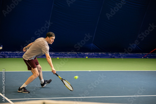 Male player in action on the indoor court playing tennis and beating the ball with a racket