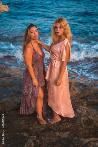 A couple of Caucasian girls in pink dresses, posing summer on the beach by the sea