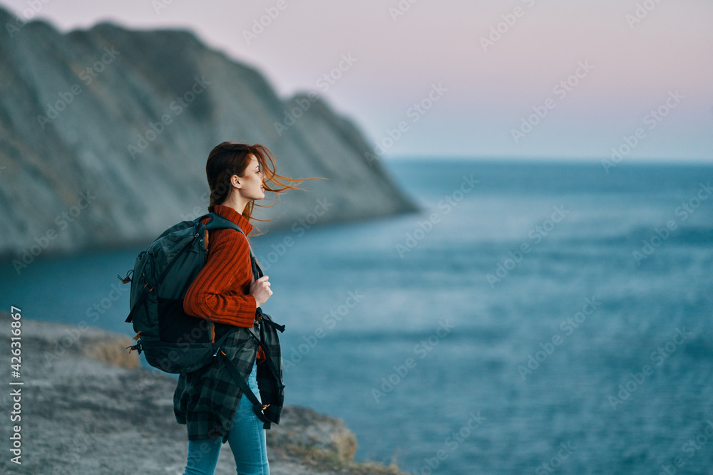Traveling with a backpack in the mountains outdoors looking at the sea red sweater jeans model