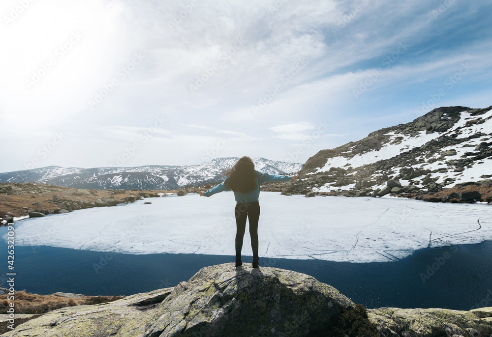 silhouette woman enjoying nature in the top of snowy mountains with a frozen lake in front of her. winter landscape