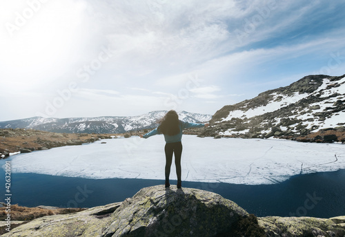 silhouette woman enjoying nature in the top of snowy mountains with a frozen lake in front of her. winter landscape