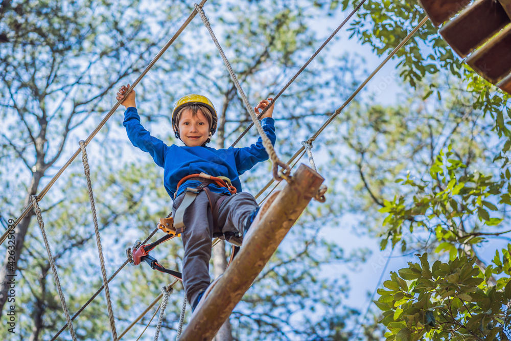 Happy child in a helmet, healthy teenager school boy enjoying activity in a climbing adventure park on a summer day