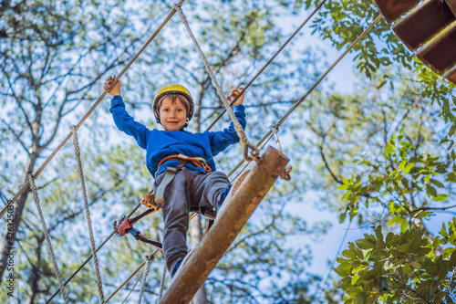 Happy child in a helmet, healthy teenager school boy enjoying activity in a climbing adventure park on a summer day