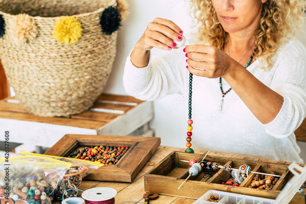 Woman at home make handmade jewellery. Box with beads on old wooden table.  view with woman