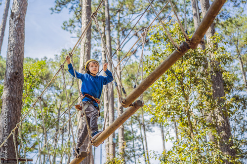 Happy child in a helmet, healthy teenager school boy enjoying activity in a climbing adventure park on a summer day