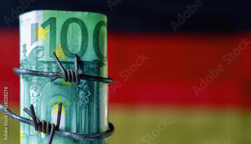 One hundred EURO bancnotes wrapped in barbed wire against flag of Germany as symbol of global economic crisis and recession. Selective focus on money. Copy space. Horizontal image. photo